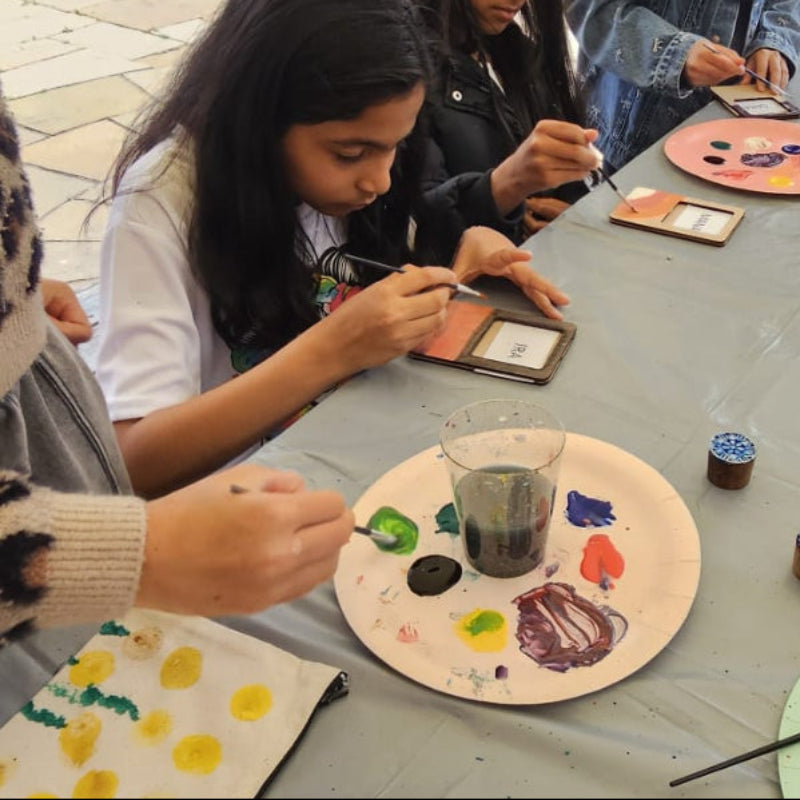 Children engaged in art activities at a table outdoors with various art supplies.