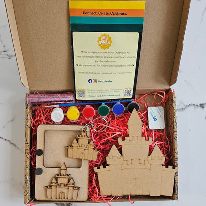 Craft kit with wooden castle pieces, paint bottles, and instructions on a marble surface.