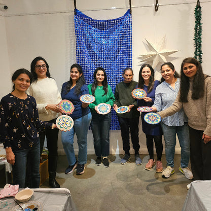 Group of people standing in a line, holding decorative mandala, with a blue patterned fabric in the background.