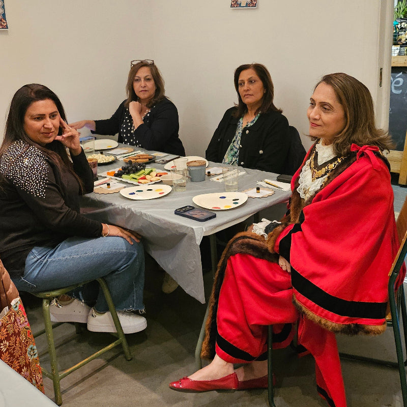 Group of women sitting around a table in a casual setting, possibly a community center.