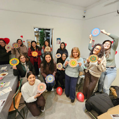 Group of women holding colourful mandala crafts in a room with balloons and a table.