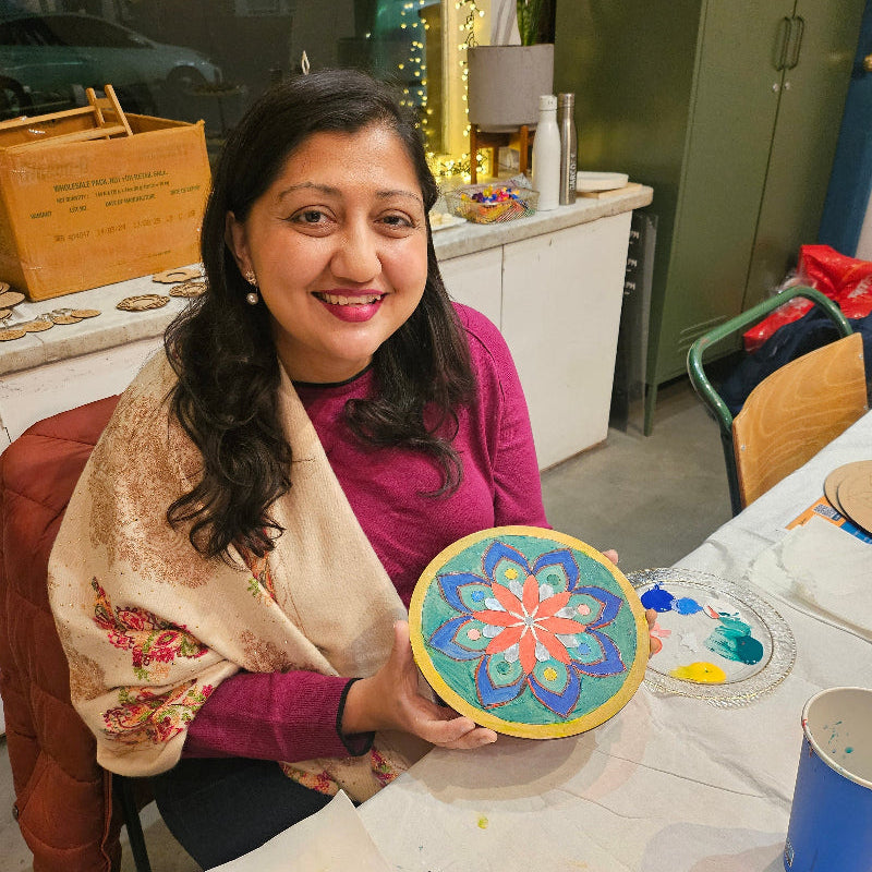 Woman holding a colourful mandala painting in a cafe setting