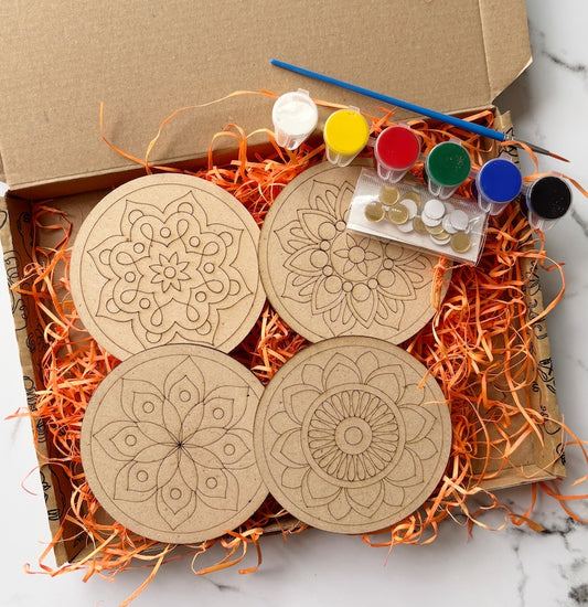 Wooden coasters with mandala designs in a box with paint supplies on a marble surface